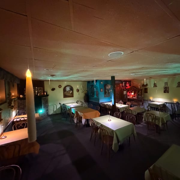 Dimly lit restaurant dining room with tables set, illuminated by candles and soft ambient lighting.