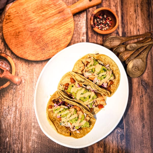 Three Señor Tomas Mexican tacos with guacamole and sauce on a white plate, on a wooden table.